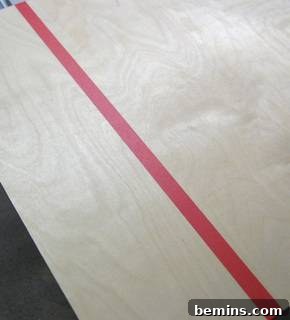 Preventing Plywood Splintering: A Guide to Clean Cuts 3 Red masking tape applied along a cut line on plywood.