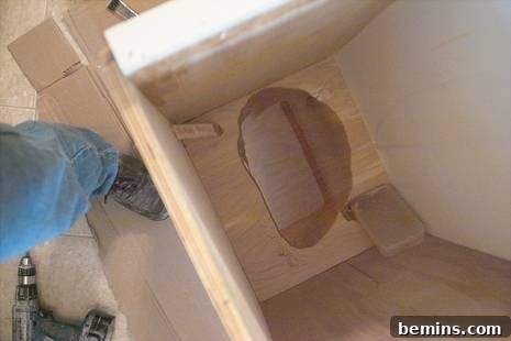 Discreet Waste Solutions 3 The initial stage of the DIY project, showing a corner of a wooden room with the birch plywood box foundation for the custom trash can, highlighting the raw materials before finishing.