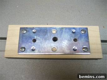Screws are placing a metal plate into wood, illustrating the attachment of the mending plate to the hardwood base for the camera mount.