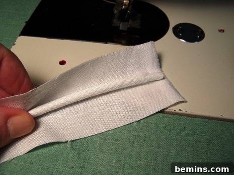 Fabric strip folded over the cord, with the raw edges aligned, ready for stitching