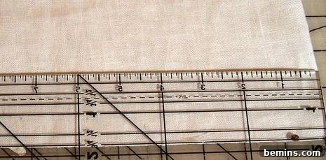 Detailed view of using a rotary cutter along a quilting ruler to cut fabric strips on the bias