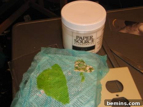 Some tissue paper, a book, a container of glue and an electrical outlet plate on a gray metal surface.