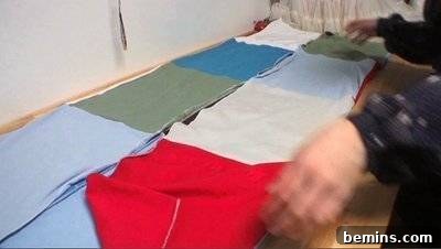 Squares of cloth cut out of old t-shirts are arranged next to each other on a table. Folding a Blanket.
