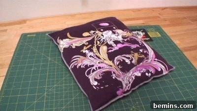A purple pillow with a pink feather design is laying on a green cutting mat. Completed Pillow.