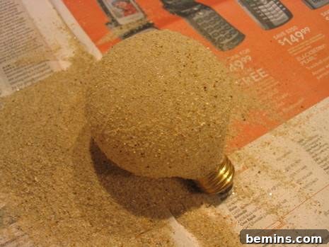 DIY Sanded Light Bulb 7 A round light bulb, coated with sand, on a piece of newspaper.