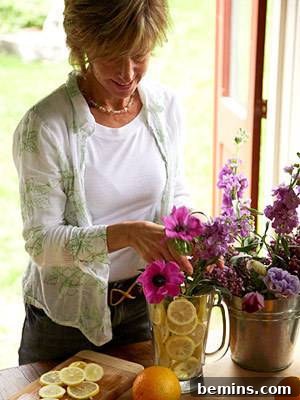Simple Citrus Slice Flower Arrangements 4 An older woman standing at a table with a series of pots and flowers in front of her, illustrating the joy and satisfaction of engaging in floral arrangement and home gardening.