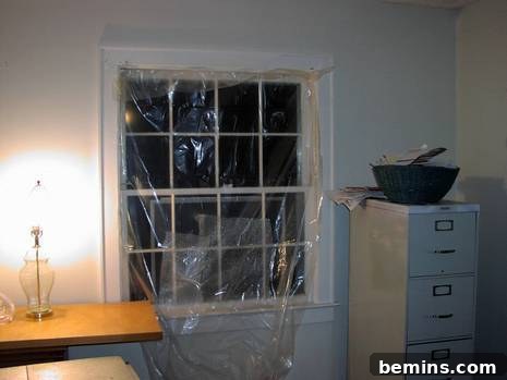 Plastic sheeting is covering a window opening in a white room, indicating missing panes and a home in the midst of renovation.