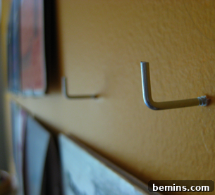 L-shape hooks have been screwed in a wall to display wall art.