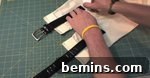 A person is measuring a black belt on a gridded surface.