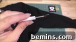 A hand holds a crafting needle, while a black sweater lays on a table, ready for alteration.