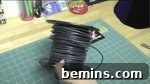 A hand holding a roll of black wire over a green mat, preparing to make the hat brim.