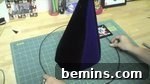 A dark blue cone inside of a dark blue circle on top of a green cutting mat, preparing to attach the brim to the hat.