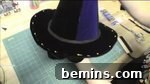 A person is working with dark colored material for a craft, sewing the fabric around the wire brim.