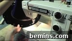 A black item being sewn on a machine, securing the fabric to the wire brim.