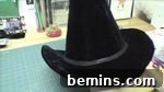 A black witch's hat sits on a green crafting mat, showcasing the completed hat with embellishments.