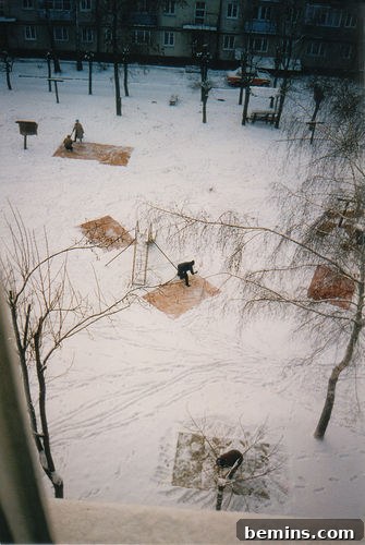 A snowy park with snow-covered picnic tables surrounded by bare trees.