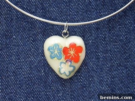 Handmade heart necklace with orange and blue flowers painted on to it. A beautiful example of cold porcelain jewelry.
