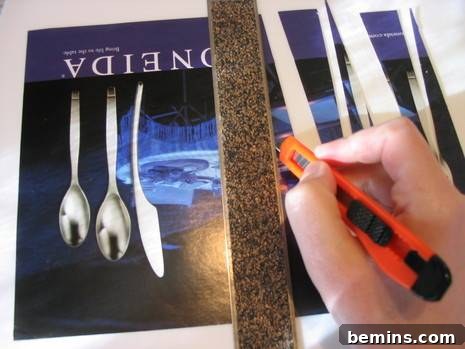 A person's hands carefully using a utility knife and a ruler to precisely cut long, triangular strips from a colorful magazine page on a cutting mat. This demonstrates the initial crucial step in preparing paper for bead making.