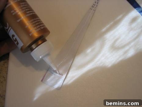 A close-up shot of a person applying a thin, consistent line of craft glue along the wrong side of a tapering paper strip, starting about three-quarters of the way up from the wide end towards the pointed tip, preparing it for rolling.