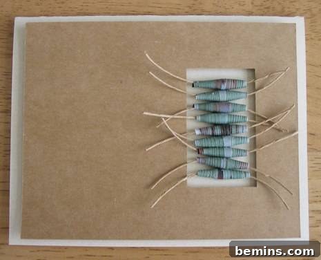 A rustic, brown-toned greeting card featuring an elegant, multi-strand design of blue and brown paper beads. The beads are arranged artfully to create a textured, three-dimensional embellishment on the card's front, offering a personalized touch.
