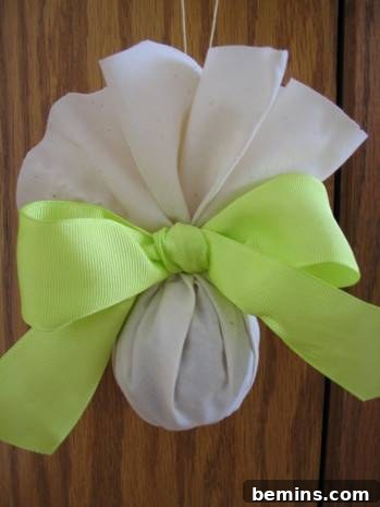 Timeless Fragrance: Crafting Pomanders 8 A finished pomander housed in white muslin fabric and held together with a light green bow, a charming and fragrant addition to any home.