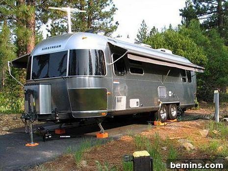 Airstream trailer parked on asphalt in a wooded area