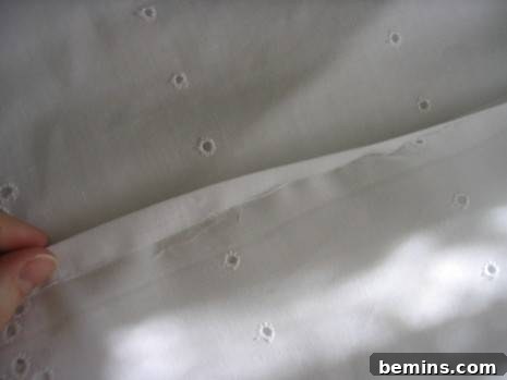 Fingers holding edge of linen cloth with eyelet holes.