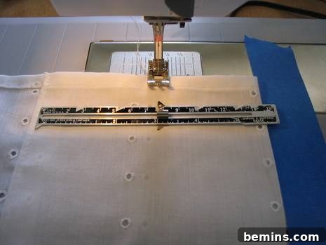 White eyelet fabric is being sewn on a sewing machine with white painter's tape on it.