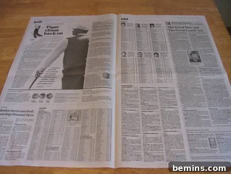 An opened newspaper spread out on a wooden table, ready to be transformed into a baseball mitt.