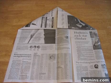 Origami art in progress using a section of newspaper, with corners folded towards the center.