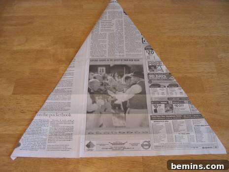 A newspaper used for origami, flipped over to the opposite side to continue the folding process.