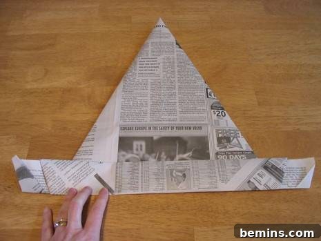 A person folding a newspaper to create a boat shape, with the bottom edge being folded upwards multiple times.