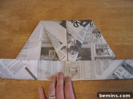 A person folding a piece of newspaper, tucking the top tip into the folded band at the bottom.