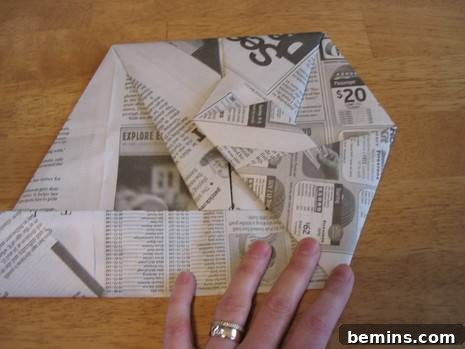 A person carefully folding a piece of newspaper to refine the shape of the origami craft.