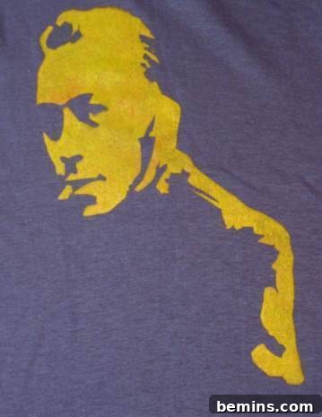 An individual carefully applying black fabric ink to a t-shirt using a handcrafted stencil and a small roller, highlighting the precision and detail of DIY textile art.