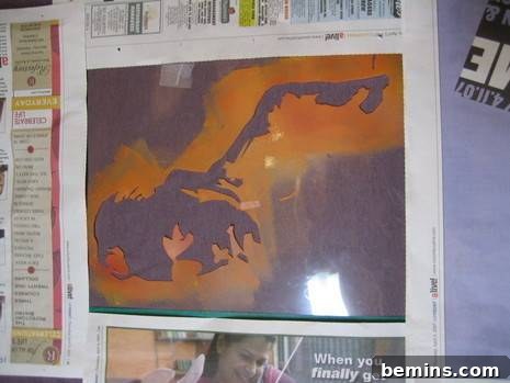 A t-shirt laid flat with a custom stencil securely fastened by masking tape and protected by newspaper, meticulously prepared for ink application in a DIY printing setup.