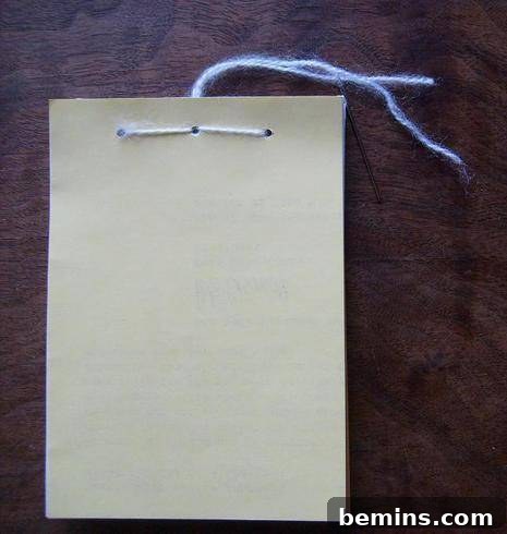 Hand sewing the stack of prepared paper pages together with yarn and a needle
