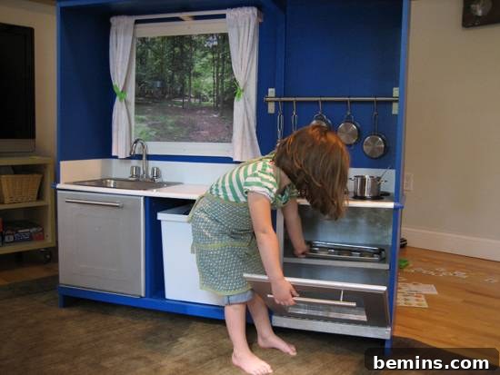 A young girl putting a cookie tray in a small oven in a blue kitchen.
