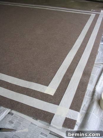 A brown rug with masking tape applied along the edges, creating a clean border for painting.