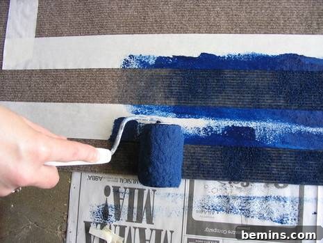 A hand using a paint sponge to apply blue paint to the rug within the taped-off area.