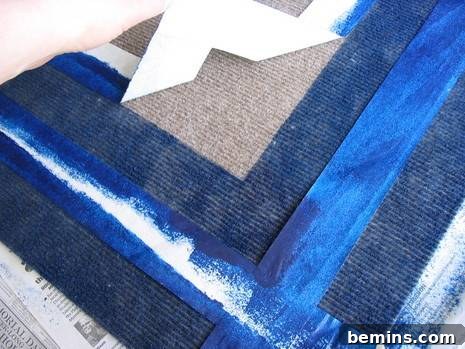 A hand peeling away the masking tape from the rug, revealing the clean edges of the painted design.