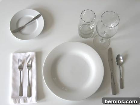 A white plate with silverware, a bread plate, a wine glass, and a water glass.