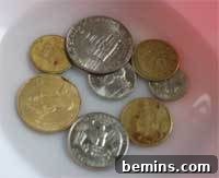 Several different coins soaking in a white dish with cleaning solution, illustrating the cleaning process.