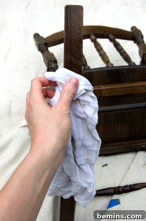 A hand gently polishing the wood surface of a rocking chair, preparing it for painting