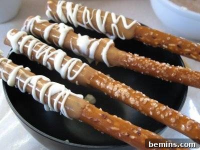 Four pretzel sticks with icing on a black plate.