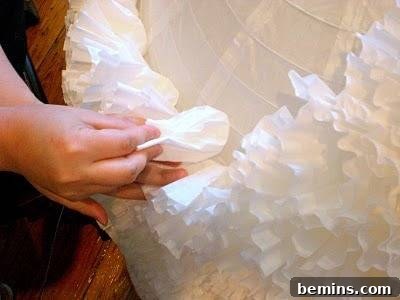 A close-up image showcasing the process of attaching white ruffles (made from coffee filters) to a lampshade.