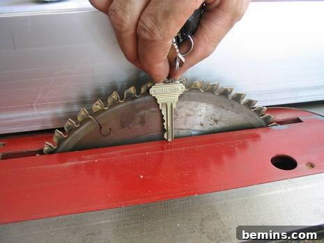 A hand holding a key next to the the saw blade on a red table saw. Illustrates setting the saw blade depth to match key thickness.