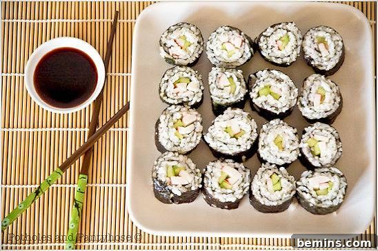 Sixteen sushi rolls sit on a white plate on a bamboo place mat.