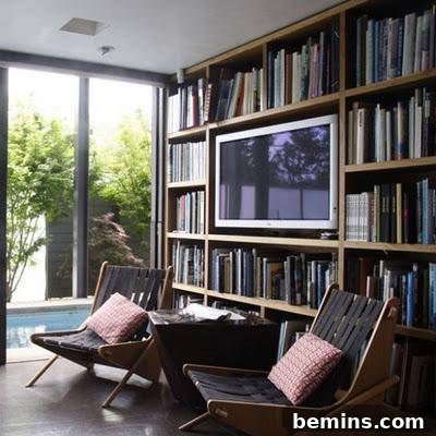 A TV is seamlessly integrated into a wall filled with books, flanked by two comfortable chairs, showcasing a balanced and stylish living space.