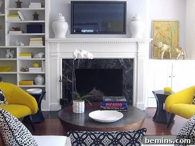 A white living room features a TV mounted above a fireplace, adorned with black and yellow decorations, creating a striking and balanced aesthetic.